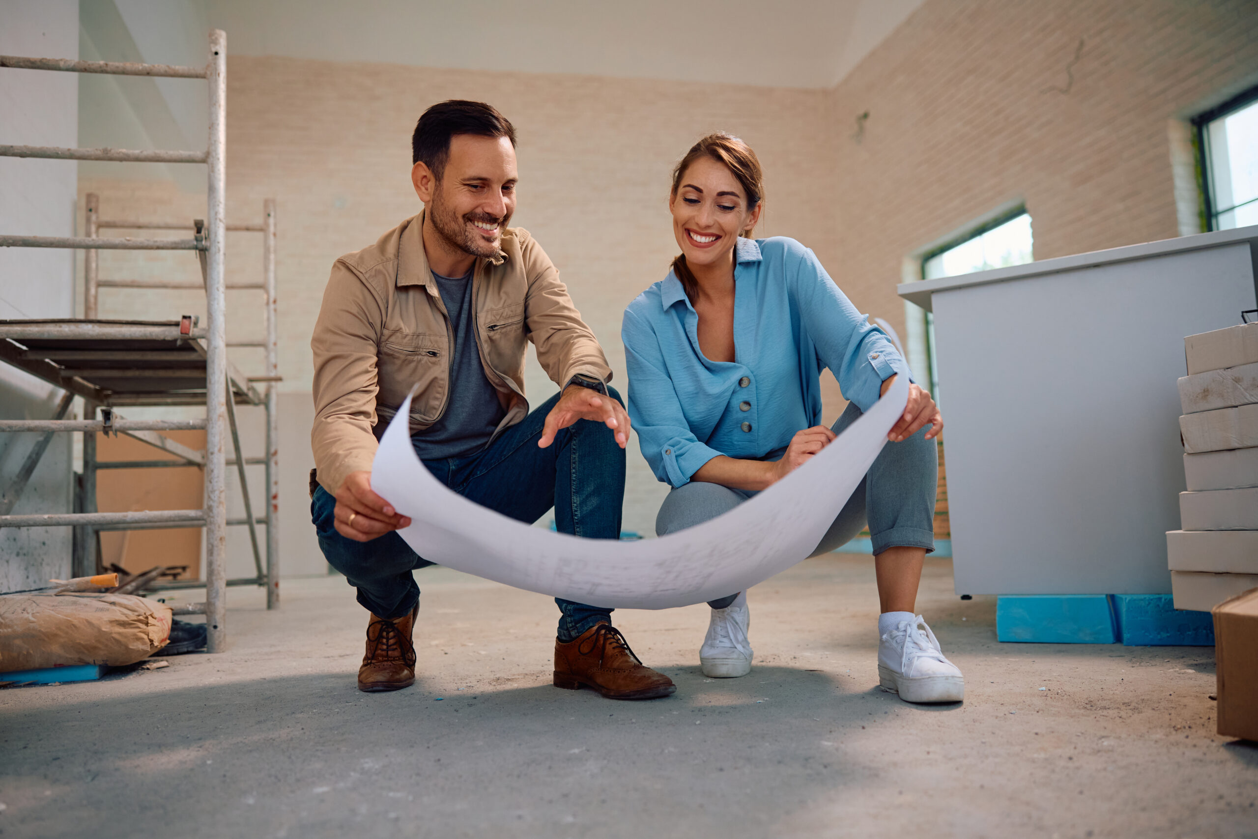 Happy couple analyzing blueprints during home renovation process.